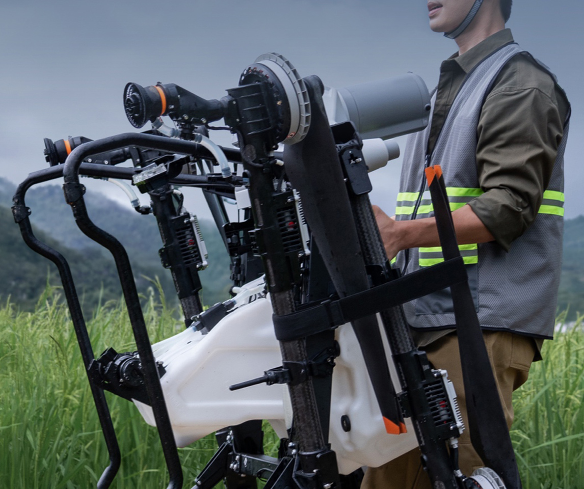 Operator carrying a folded DJI Agras T55 on the new transport handle across a grass field