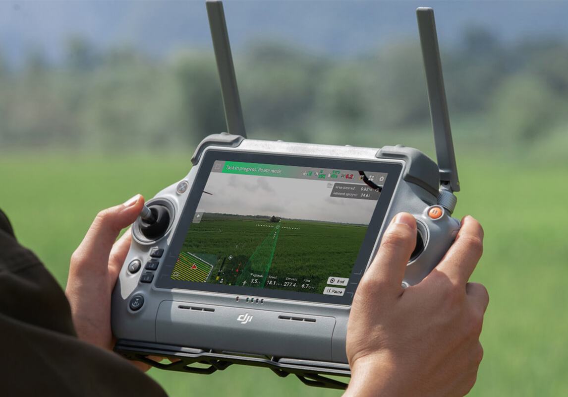 Operator holding the DJI RC Plus 2 AG remote controller showing a field route on its screen