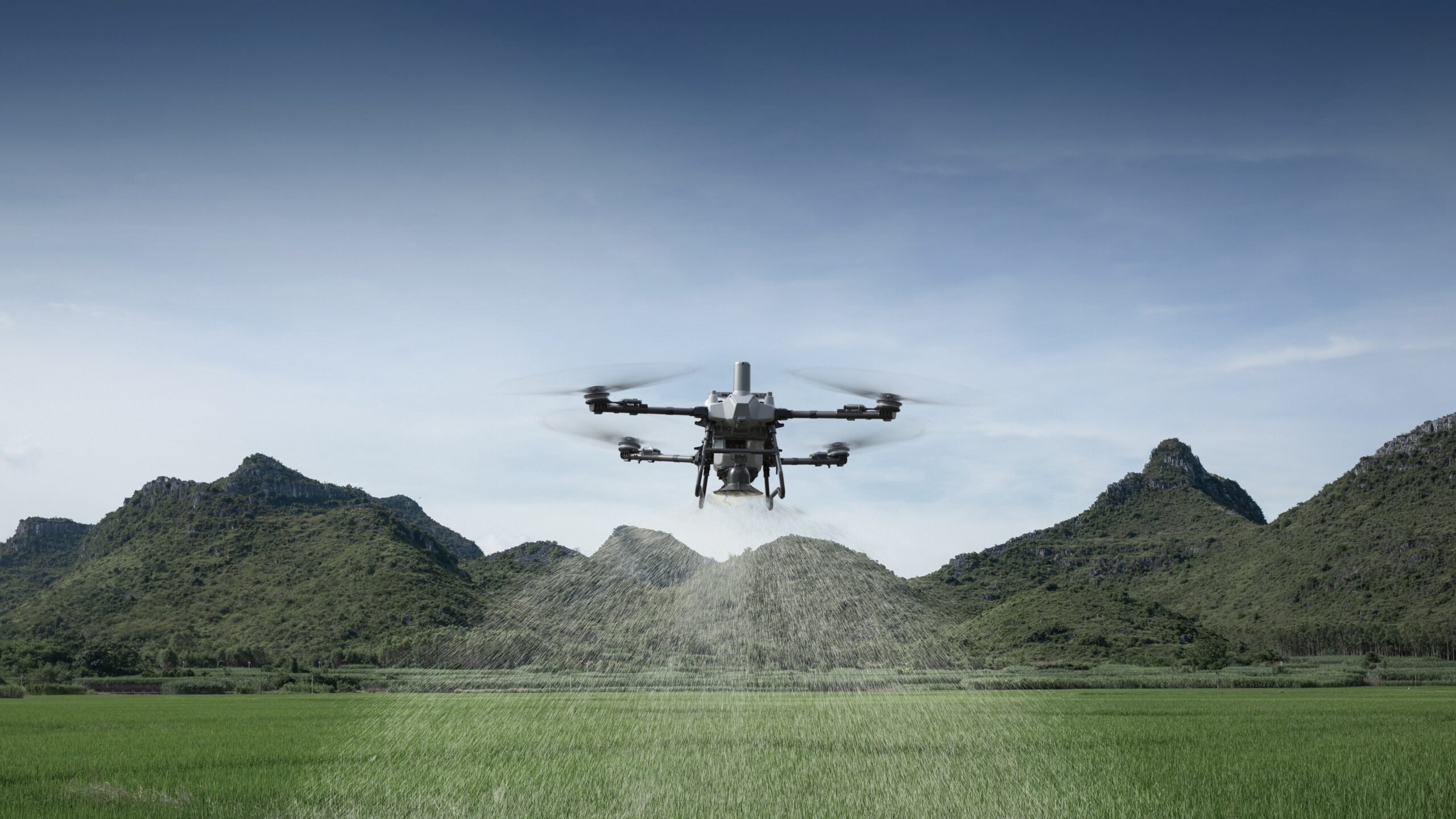 DJI Agras T55 spreading granules over a green paddock with hills behind